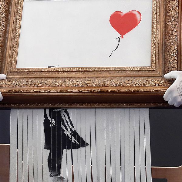 Två män sätter upp Banksys konstverk på en vägg.