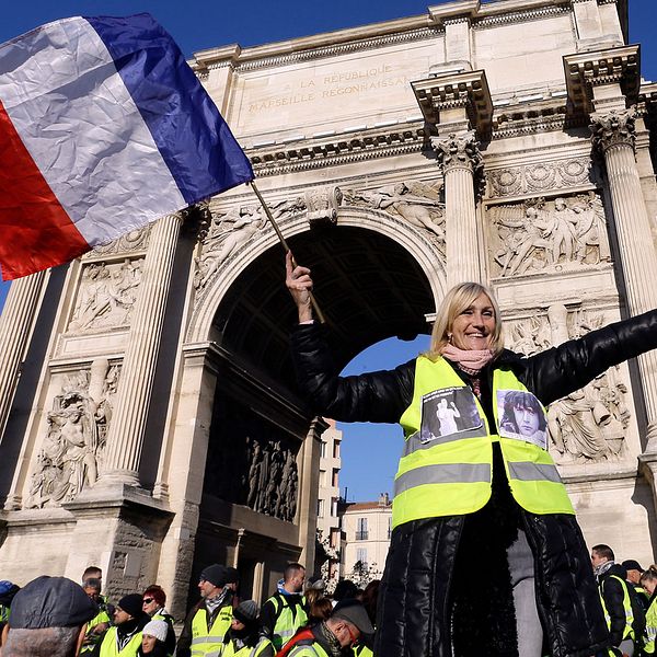 En demonstrant i gul väst viftar med den franska flaggan framför Triumfbågen i Marseille