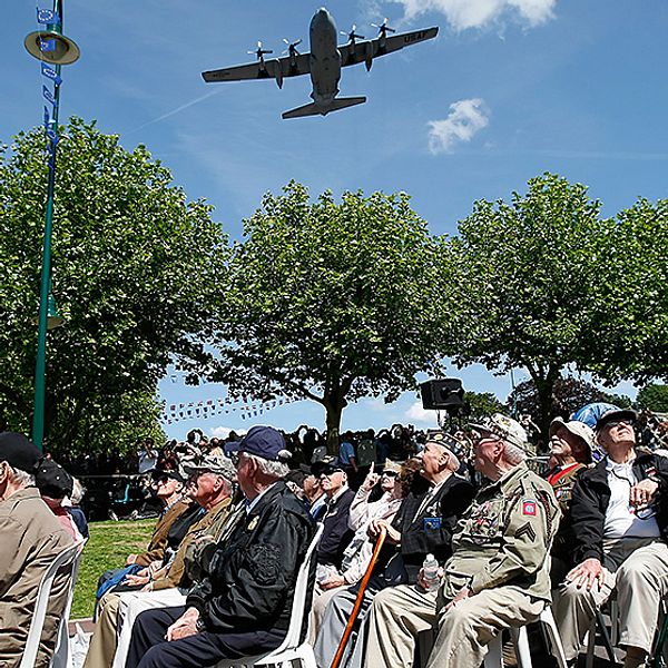Amerikanska krigsveteraner tittar upp mot ett C130 Air Force-plan som flyger över Sainte-Mere-Eglise i Frankrike under en ceremoni för att hedra fallskärmshoppare.