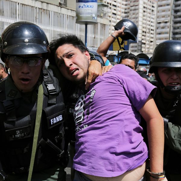 Militärpolis håller venezuelan kring halsen under demonstration.