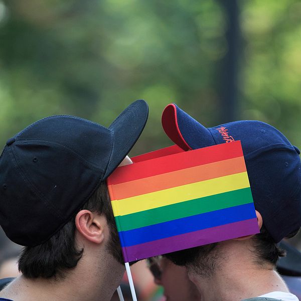 Två män kysser varandra bakom en regnbågsflagga.