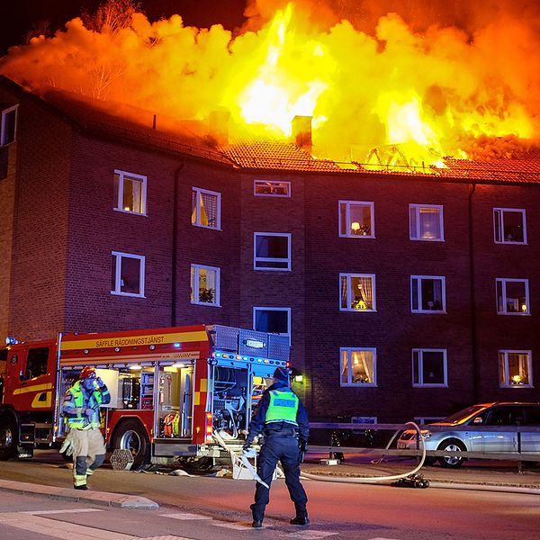 Husets tak som brinner. På gatan finns polis och brandkår.