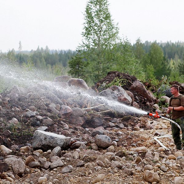 Brandman med vattenslang ute i skogen.