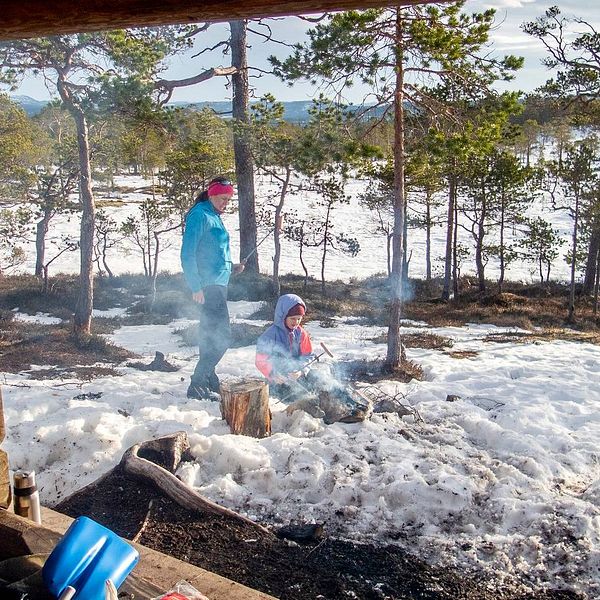Kvinna och barn grillar korv i snön vid ett vindskydd