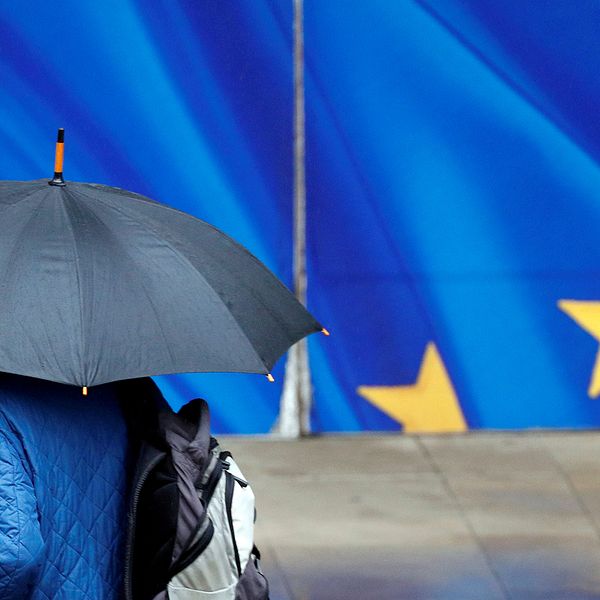 En man med paraply går för en EU-flagga.
