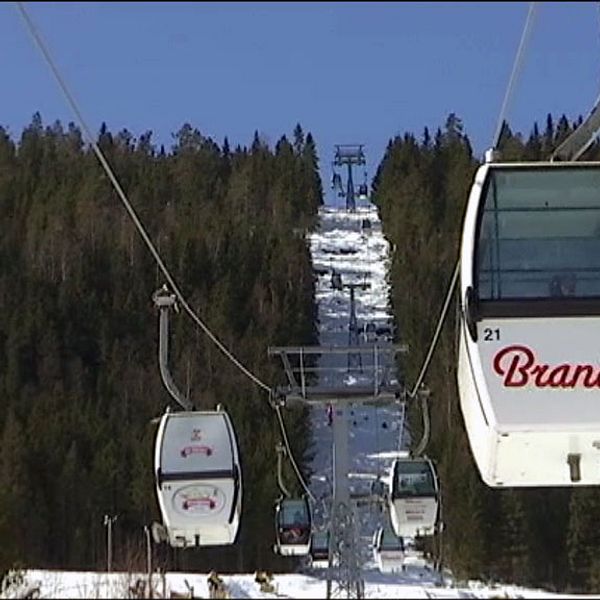 En kabinlift som det står Branäs på. I bakgrunden gröna granar och på marken vit snö.