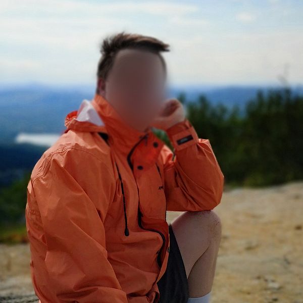 Man som sitter på en sten i naturen. Lutar huvudet i ena handen och har orange jacka.