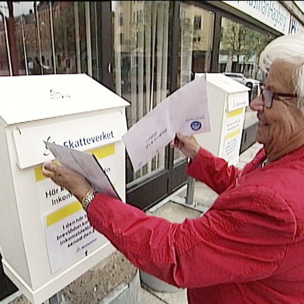 Ingrid Blomen i rödjacka och glasögon lägger ner sin pappersdeklaration i en av Skatteverkets två brevlådor.