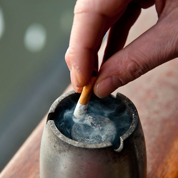närbild hand som fimpar en cigarett i askkopp
