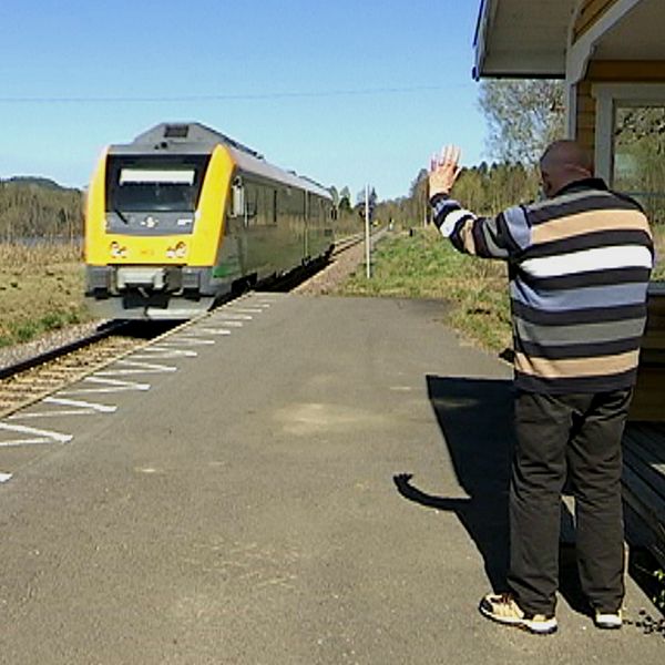 Äldre man vinkar åt ett förbipasserande tåg vid Oleby station.