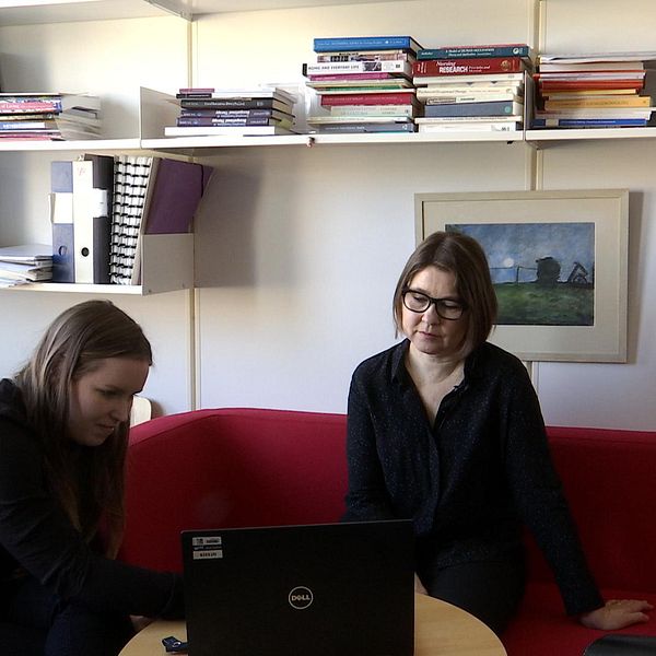 En bild på reportern som visar ett reportage för en forskare. De sitter på ett kontor med en röd soffa.