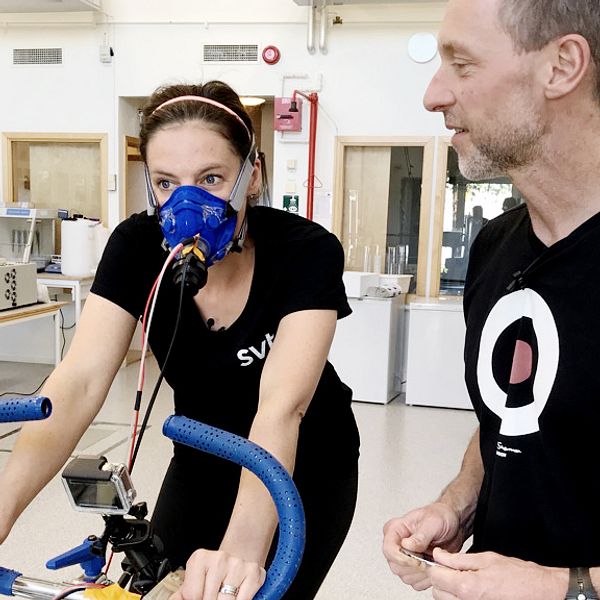 Malin Gotlin på en träningscykel. På sig har hon en andningsmask och en svart SVT-tröja.