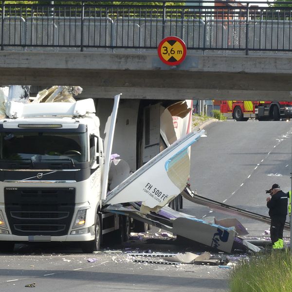 En lastbil sitter fast mitt under järnvägsbron. Sidorna på lastbilen har slagits sönder och ligger utfläkta över asfalten.