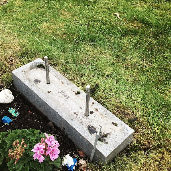 En vält gravsten. Bredvid står en ljuslykta och det ligger ett stenhjärta framför gravstenens fäste i marken.
