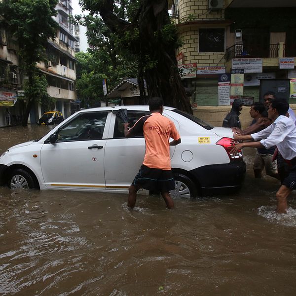 Några män knuffar en bil på en översvämmad väg.