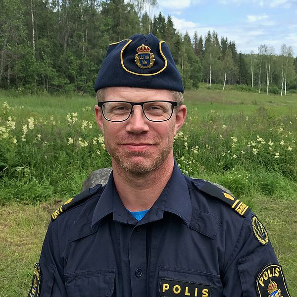 porträttbild på en man i polisuniform framför en äng med skog i bakgrunden