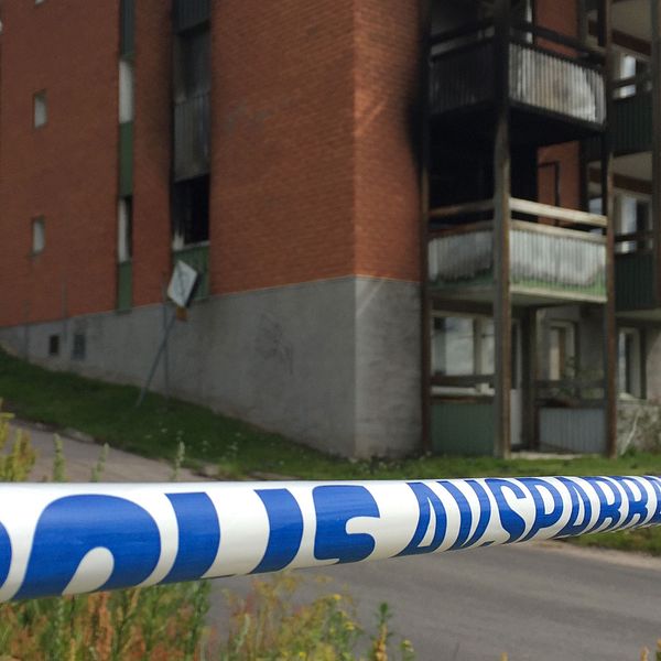 Polisens avspärrningsband i förgrunden. I bakgrunden syns ett brandskadat lägenhetshus.