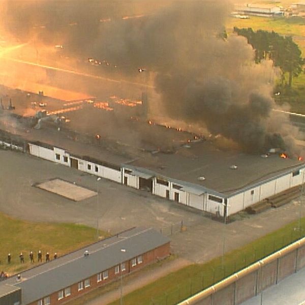 Flygbild över Tidaholmsanstalten i brand den 23 juli 1994, längst ner t v föser beväpnad polis in fångarna som gett upp
