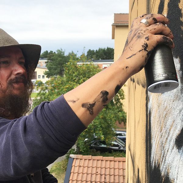 Charlie Granberg målar en husvägg med en sprejburk.