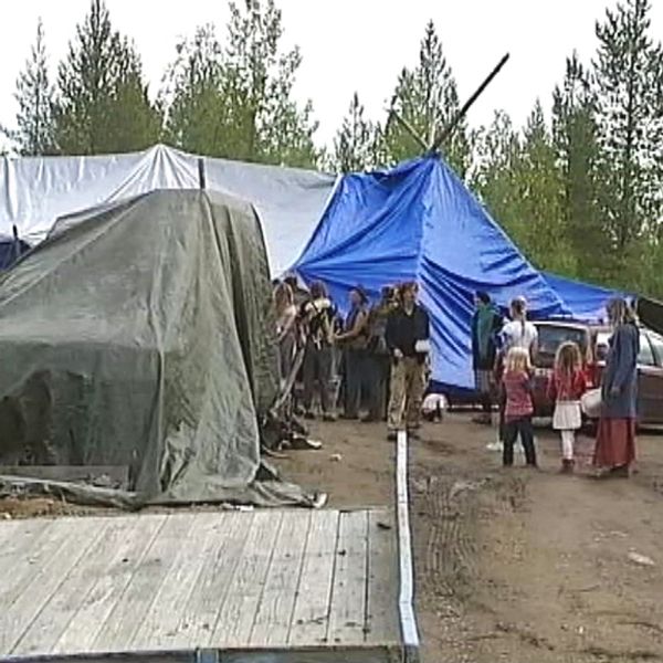 några personer på öppen plats i skogen, presenningar uppspända som tält-tak.