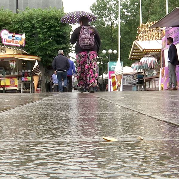 Besökare på Södertäljefestivalen i regn och i mitten promenerar en dam med paraplymellan matstånden.