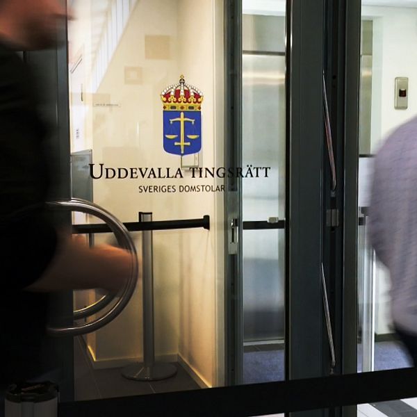 Två personer passerar förbi dörr med text ”uddevalla tingsrätt”