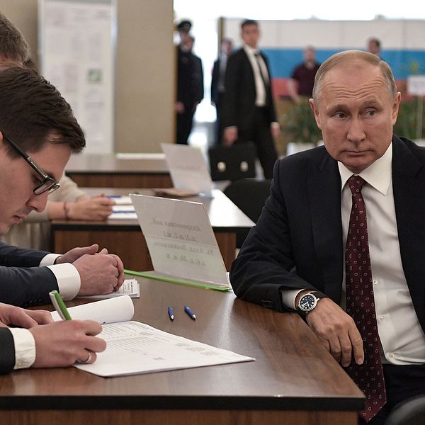 Ryske presidenten Vladimir Putin sitter vid ett skrivbord och väntar på att valförrättare ska registrera honom.