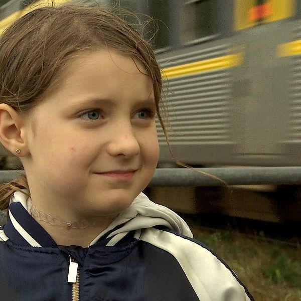 Åttaårig flicka vid järnvägsövergång. Ett tåg passerar bakom henne.