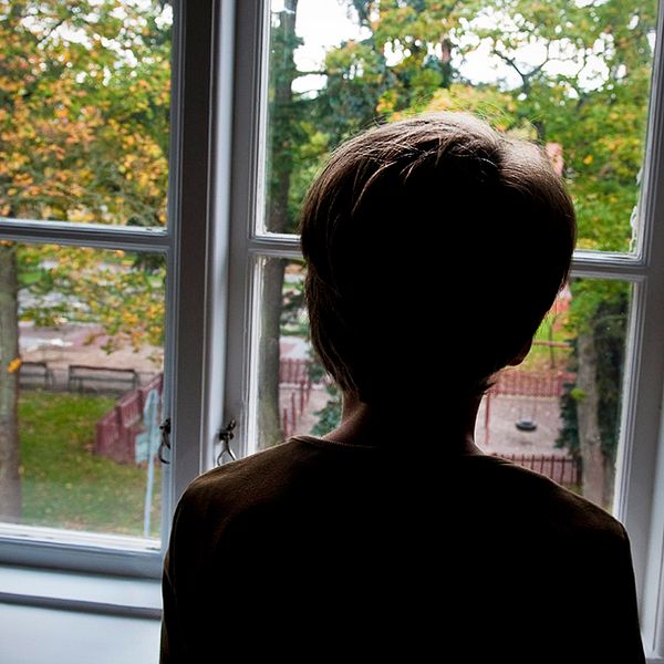 En anonym pojke tittar ut genom ett fönster.