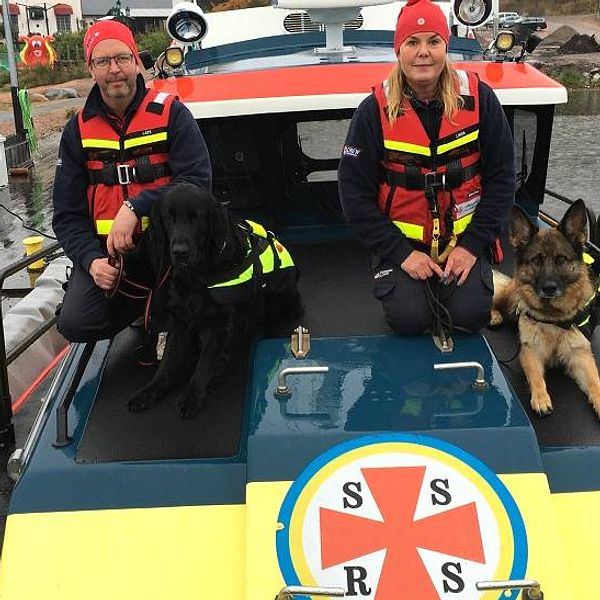 en man och en kvinna i flytvästar poserar på fören av en båt med två hundar
