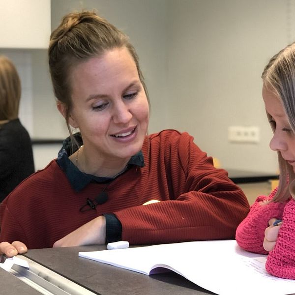 Lärarstudenten Anna Wik Maimu sitter på huk och hjälper en elev vid en skolbänk.