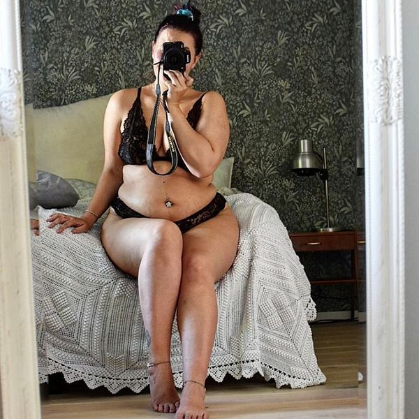 Sofia Anderberg sitter på en säng och tar en bild in i spegeln, hon har svarta underkläder på sig.