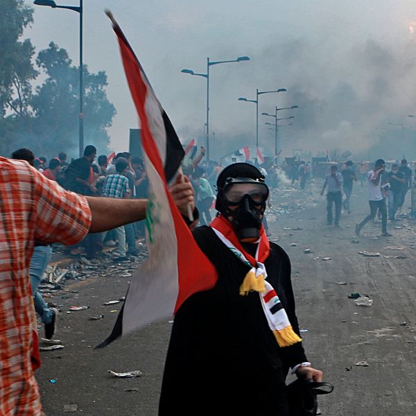 Demonstranter som tar skydd när säkerhetsstyrkor skjuter tårgas mot dem i Bagdad under måndagen.