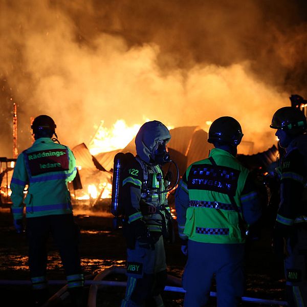 räddningspersonal framför resterna av en brinnande byggnad