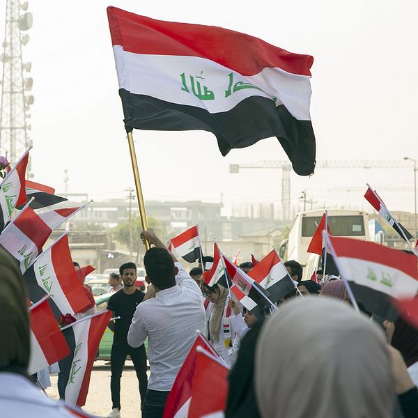 Demonstranter i Irak håller upp den irakiska flaggan.