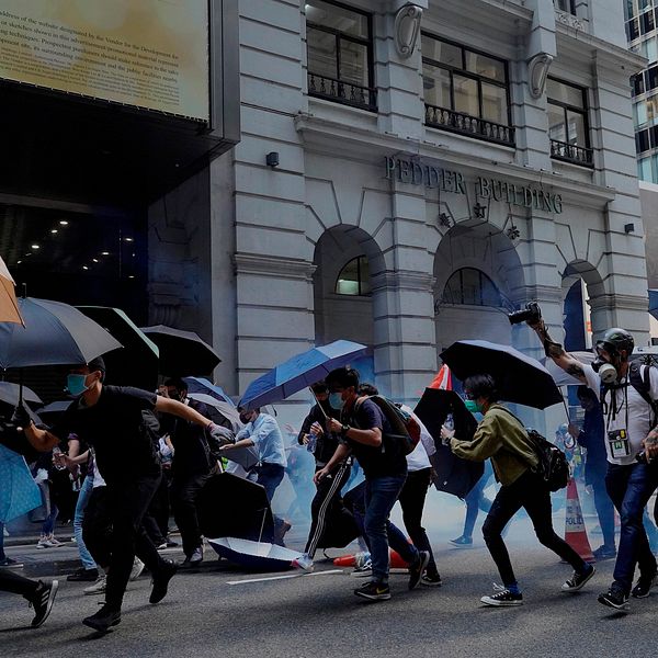 Protestanter med paraplyn beskjuts av polisen med tårgas under måndagen i Hongkong.