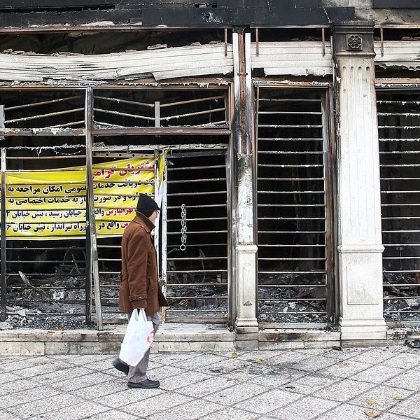 En man passerar en utbränd bank som stacks i brand under iranska protester mot höjda bränslepriser.
