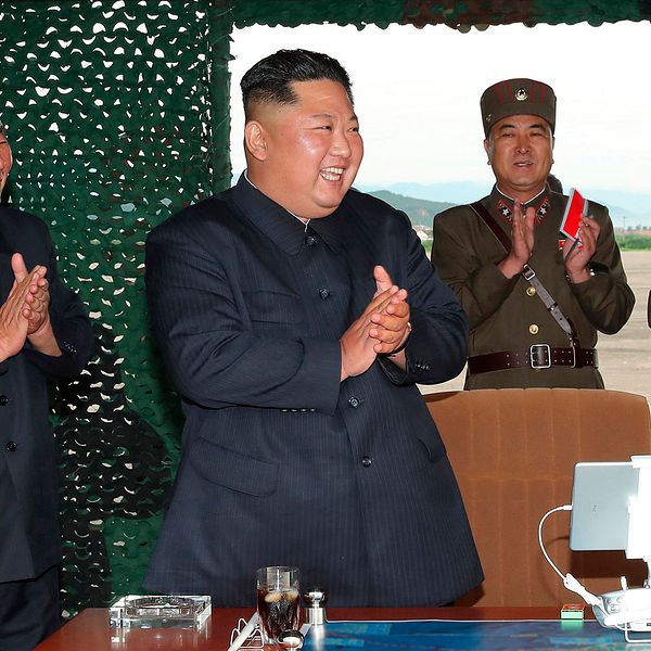 Nordkoreas ledare Kim Jong-Un omgiven av applåderande militärer vid ett skrivbord.