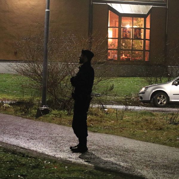 Polis står på brottsplats, bil och hus syns också i bild.