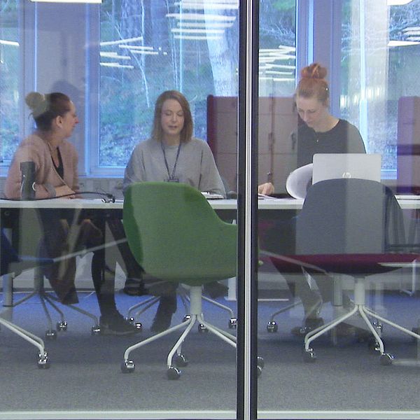 Tre kvinnor sitter vid ett konferensbord. Syns genom glasvägg.