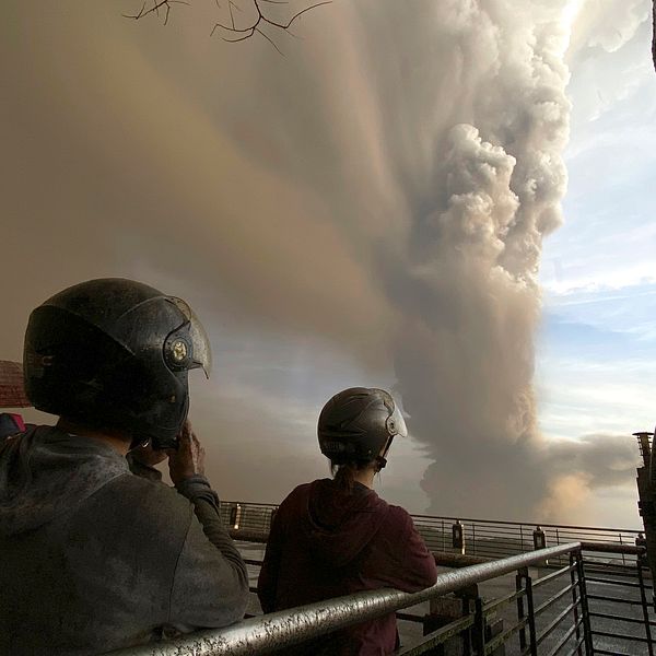 Två personer tittar på pelaren av aska och rök som stiger mot himlen.