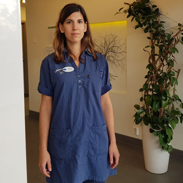 Bild på Therese Mårtensson, i läkarkläder, står i entrén till vårdcentralen.