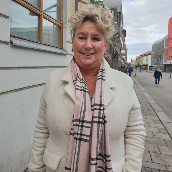 Anette står på en gata i Linköping, klädd i ljus kappa.