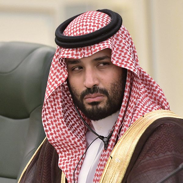 En bild på saudiske kronprinsen i traditionell saudisk klädsel sittandes i ett stol vid ett konferensbord.