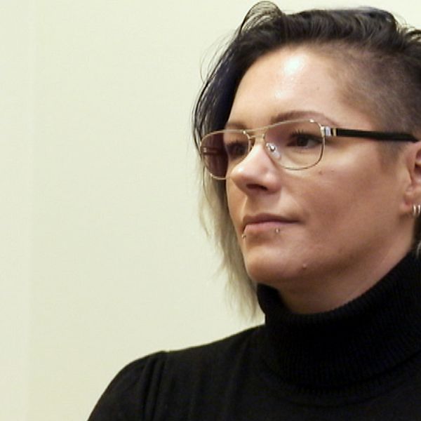 En kvinna i svart tröja och glasögon sitter mot en vit bakgrund.