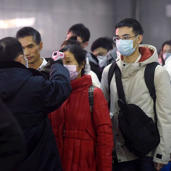 Personal använder termometer för att kontrollera temperaturen på passagerare som anländer från Wuhan på en tågstation i Hangzhou.