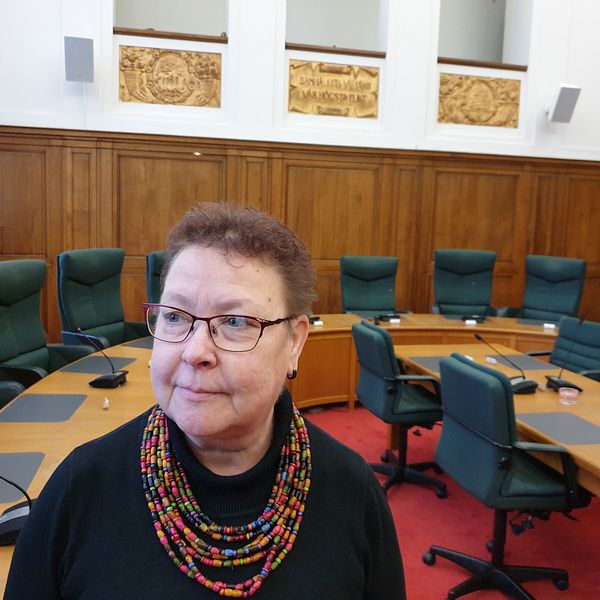 Mia Sköld står i kommunstyrelsens sammanträdesrum med ett runt bord och gröna stolar i bakgrunden.