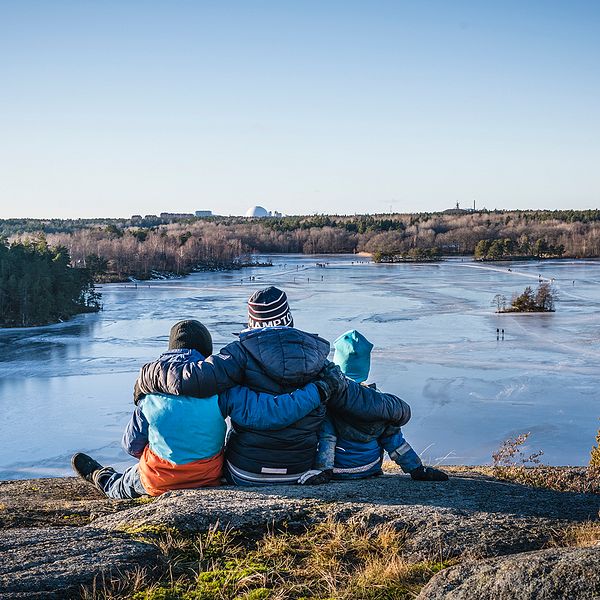 Tre personer sitter på klippa med utsikt över sjö.