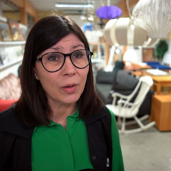 en kvinna med mörkt hår och svartbågade glasögon intervjuas i second hand-butik