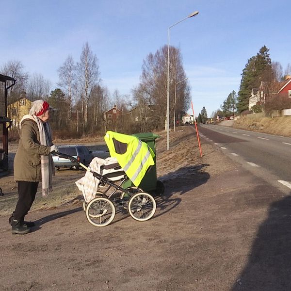 Kvinna försöker ta sig över en väg med barnvagn, bil kör förbi.